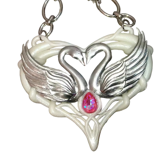 Silver necklace with a heart-shaped pendant featuring two swans and a pink gemstone on a metallic surface.