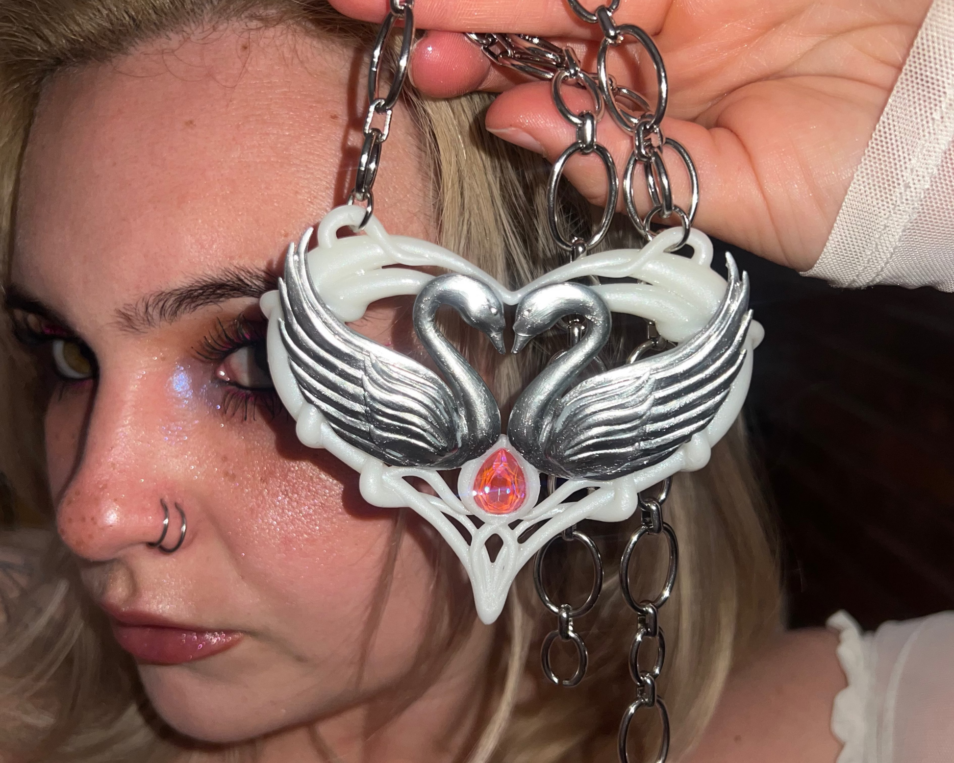 Silver necklace with a heart-shaped pendant featuring two swans and a pink gemstone on a metallic surface.