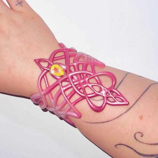 Pink bracelet with a yellow gemstone on a wrist against a white background